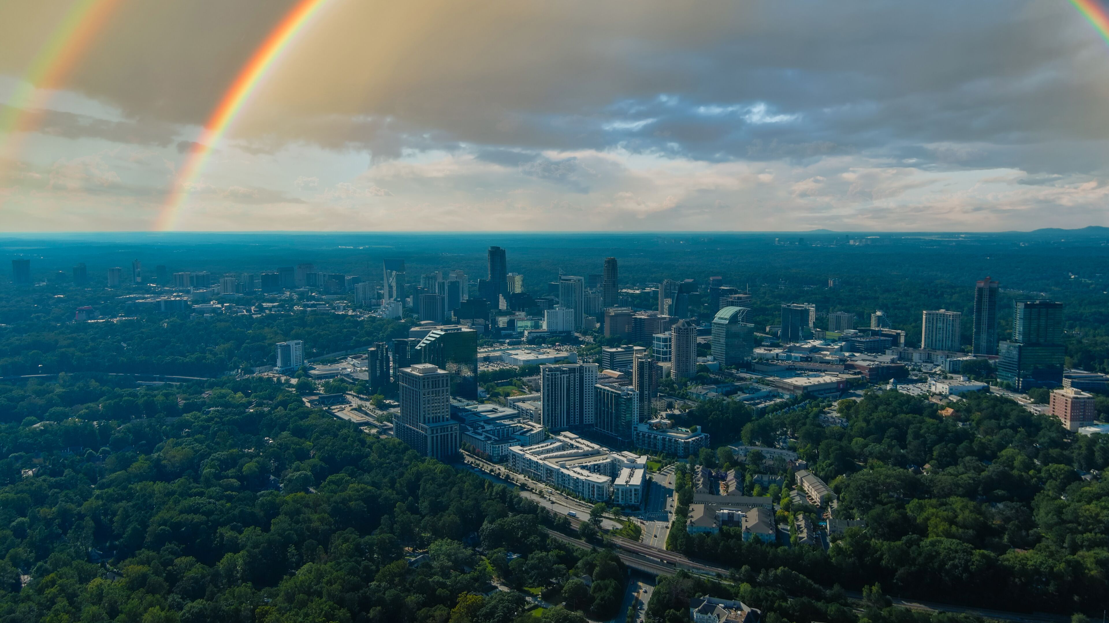A cityscape with a rainbow, dense greenery, and a mix of modern and older buildings.