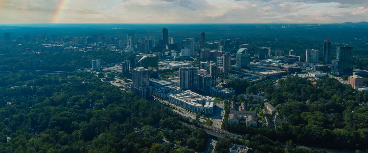 A cityscape with a rainbow, dense greenery, and a mix of modern and older buildings.