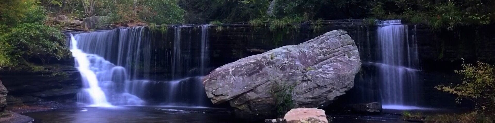 A waterfall with multiple cascades surrounded by dense forest and autumn-colored trees.