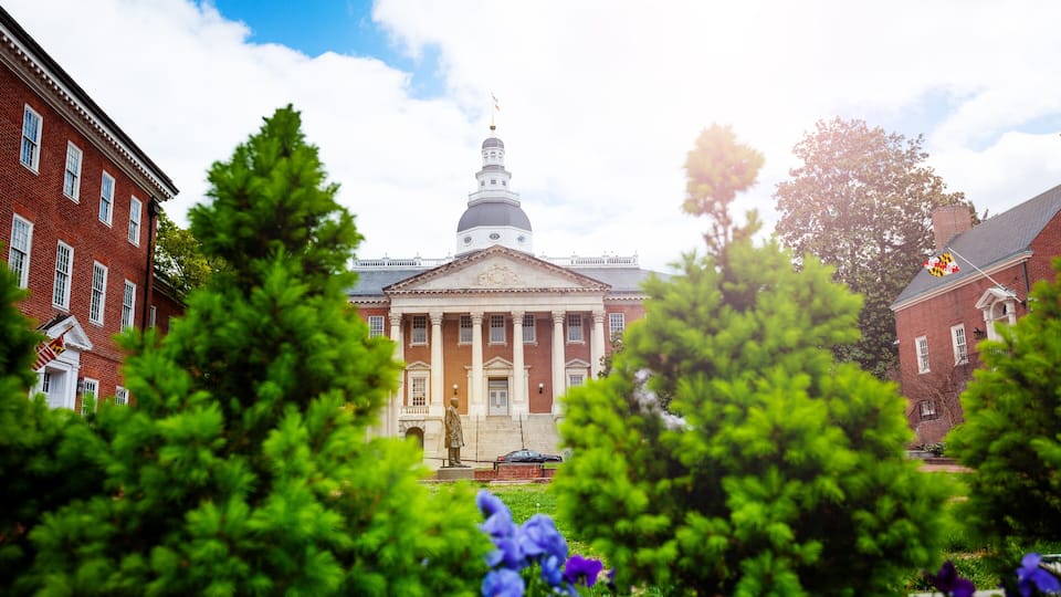 A historic building with a dome and columns, surrounded by lush greenery and flowers.
