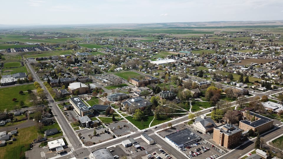 An aerial view of a town with a central square, surrounding buildings, and green fields.