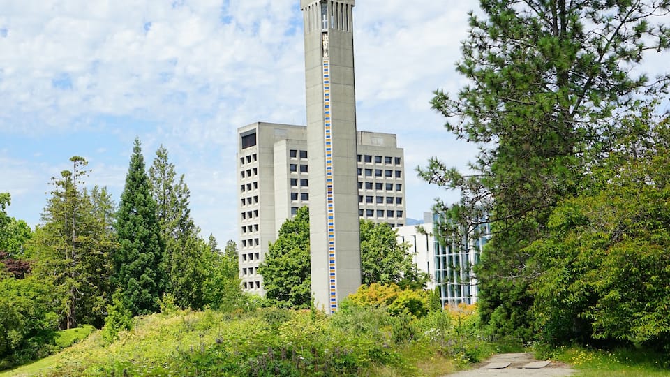 A clock tower surrounded by greenery and buildings.