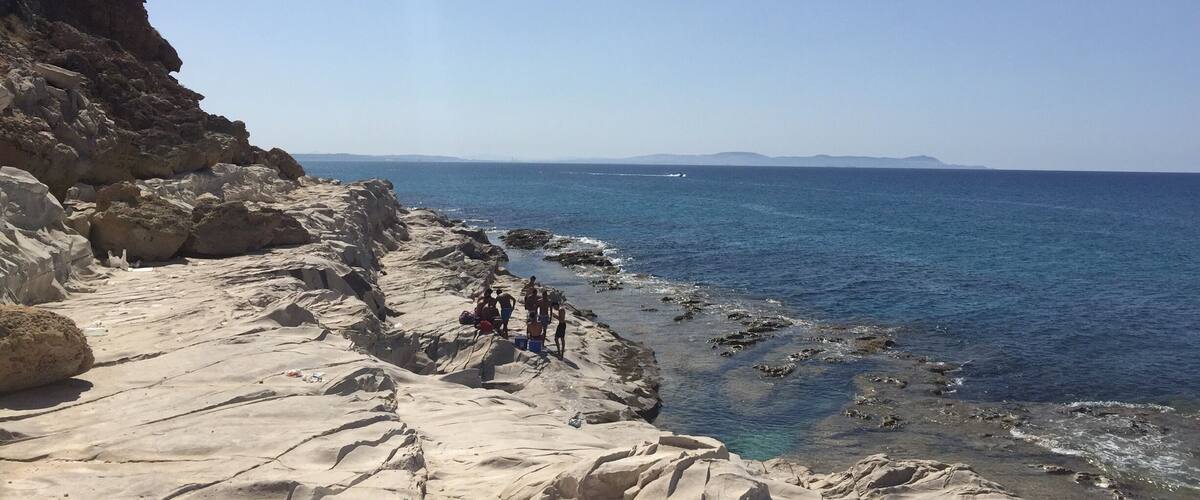 A rocky coastline with clear blue waters and distant mountains.
