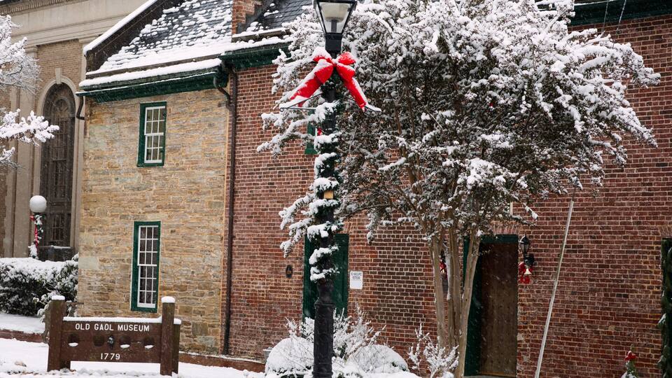 A brick building with a green window, a snow-covered street lamp, and a sign reading 'Old Gaol Museum 1779.'