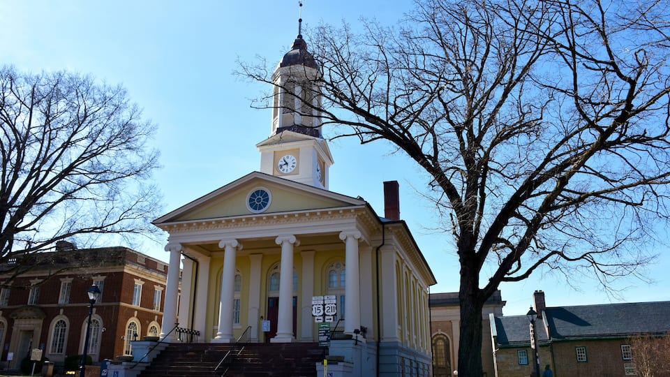 A historic building with a clock tower, columns, and a staircase leading to the entrance.