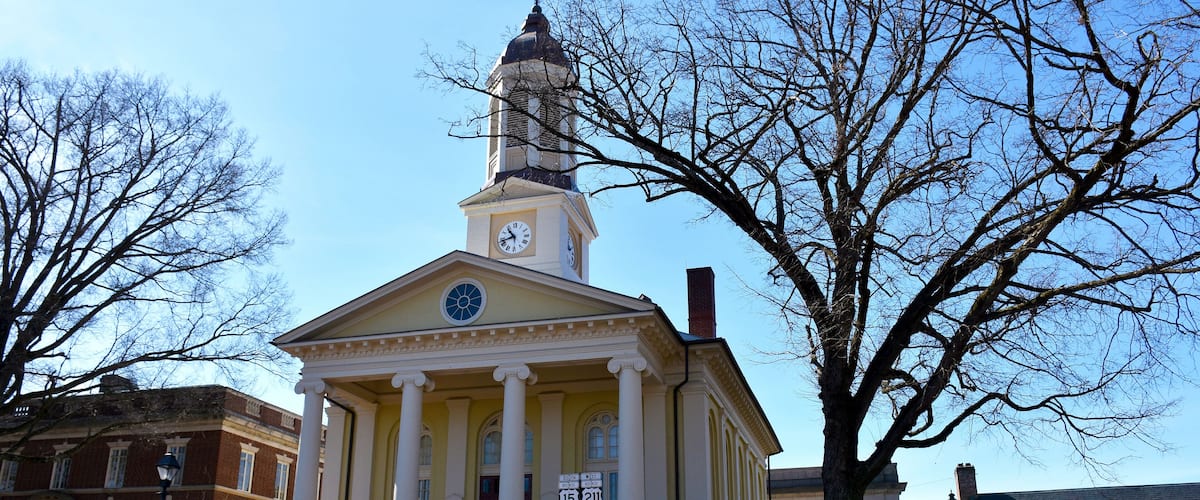 A historic building with a clock tower, columns, and a staircase leading to the entrance.