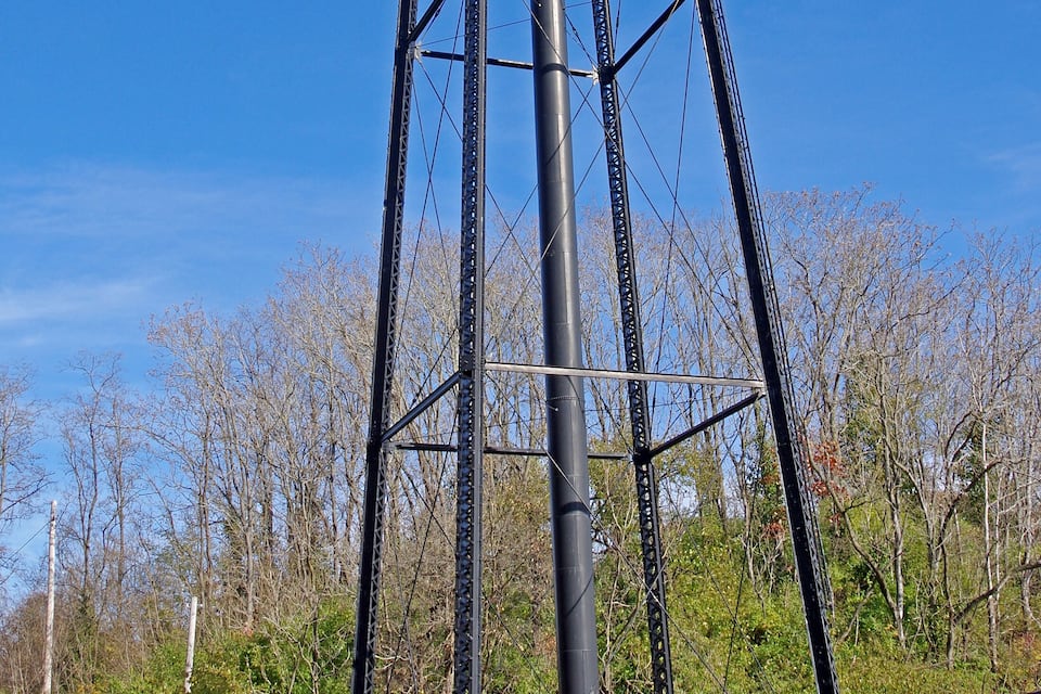 A tall water tower with a red and white striped top, surrounded by trees and a clear blue sky.