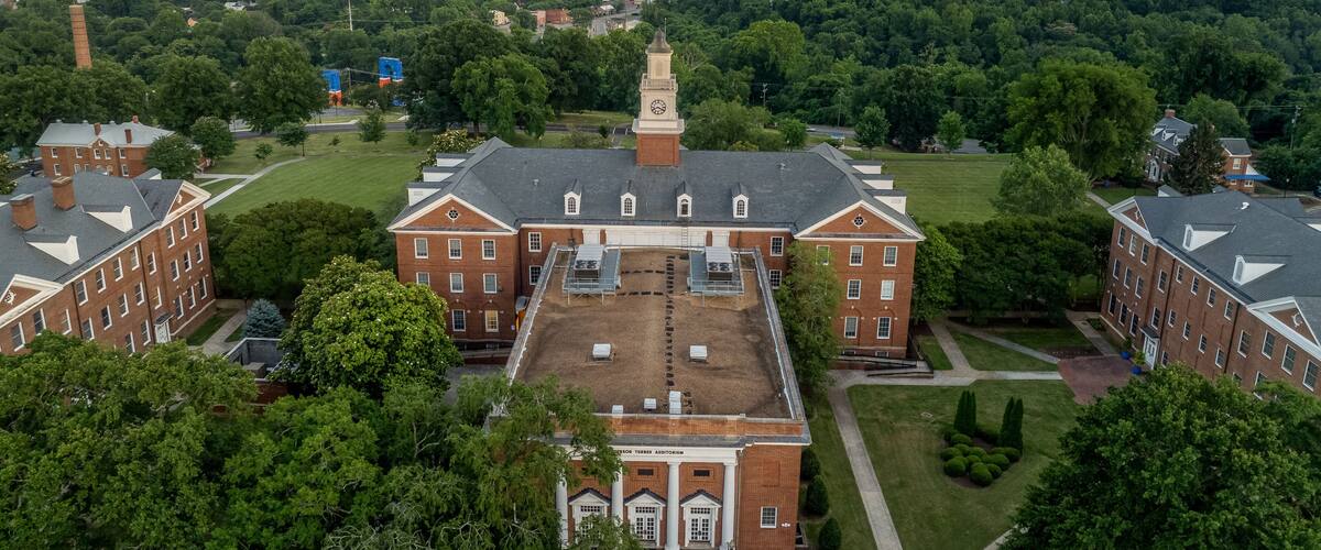 A large brick building with a clock tower, surrounded by green trees and a sunset sky.