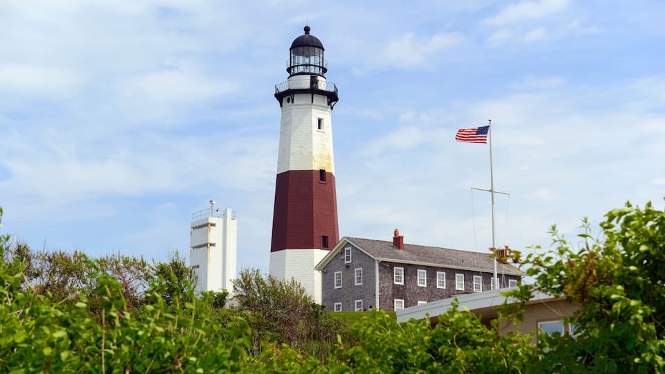 A lighthouse with a white and red tower, a flag, and a building with a gray roof.