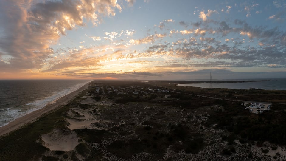 A coastal landscape with a beach, rocky terrain, and a distant power line tower.