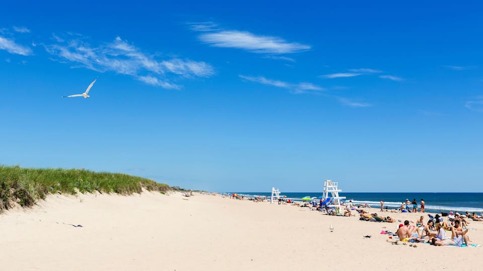 A sandy beach with people sunbathing and a lifeguard tower.