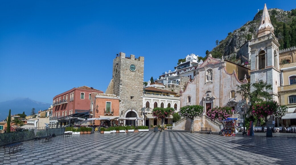 Panoramic view of Taormina main square (Piazza IX Aprile) with San Giuseppe Church, the Clock Tower and Mount Etna Volcano on background - Taormina, Sicily, Italy