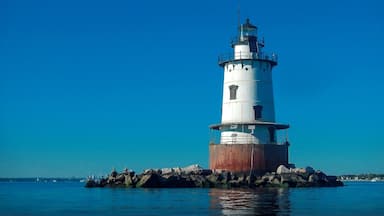 Ein weißer Leuchtturm mit schwarzer Spitze, der auf einem Felsen im Wasser steht.