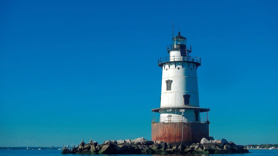 A white lighthouse with a black top, situated on a rocky outcrop in the water.