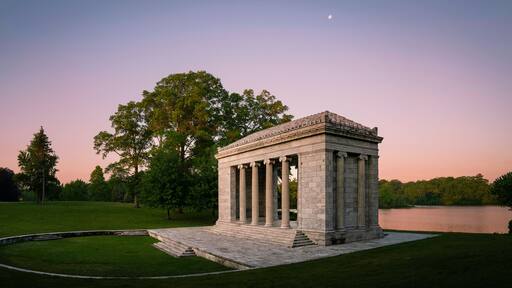 Tranquil sunset moon rising landscape at Temple to Music Pavilion and meadow forest park at Roger Williams Park in Providence, Rhode Island, pink horizon and water reflections on Cunliff Lake