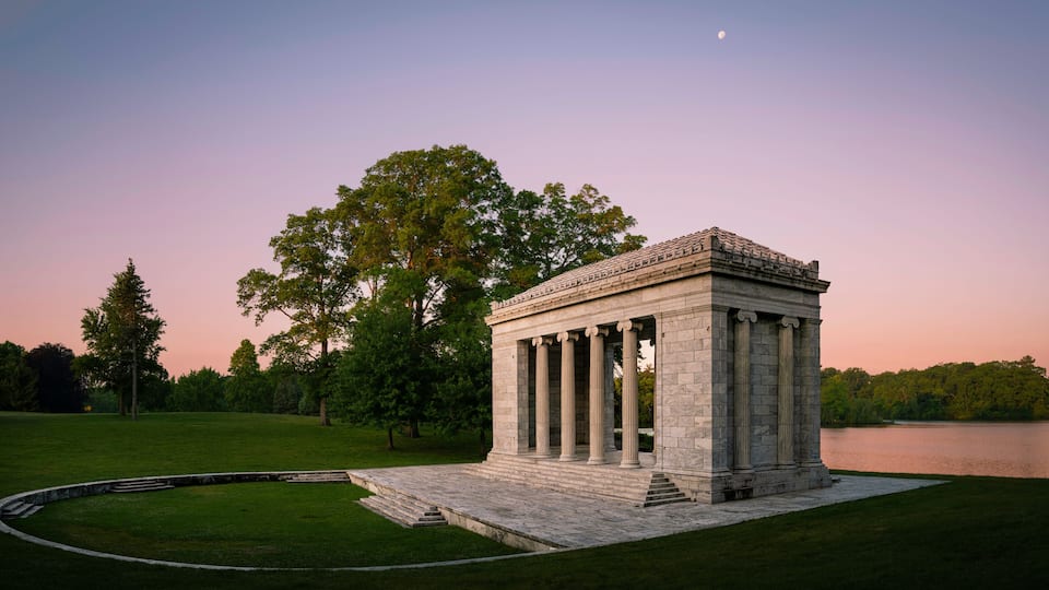 Tranquil sunset moon rising landscape at Temple to Music Pavilion and meadow forest park at Roger Williams Park in Providence, Rhode Island, pink horizon and water reflections on Cunliff Lake