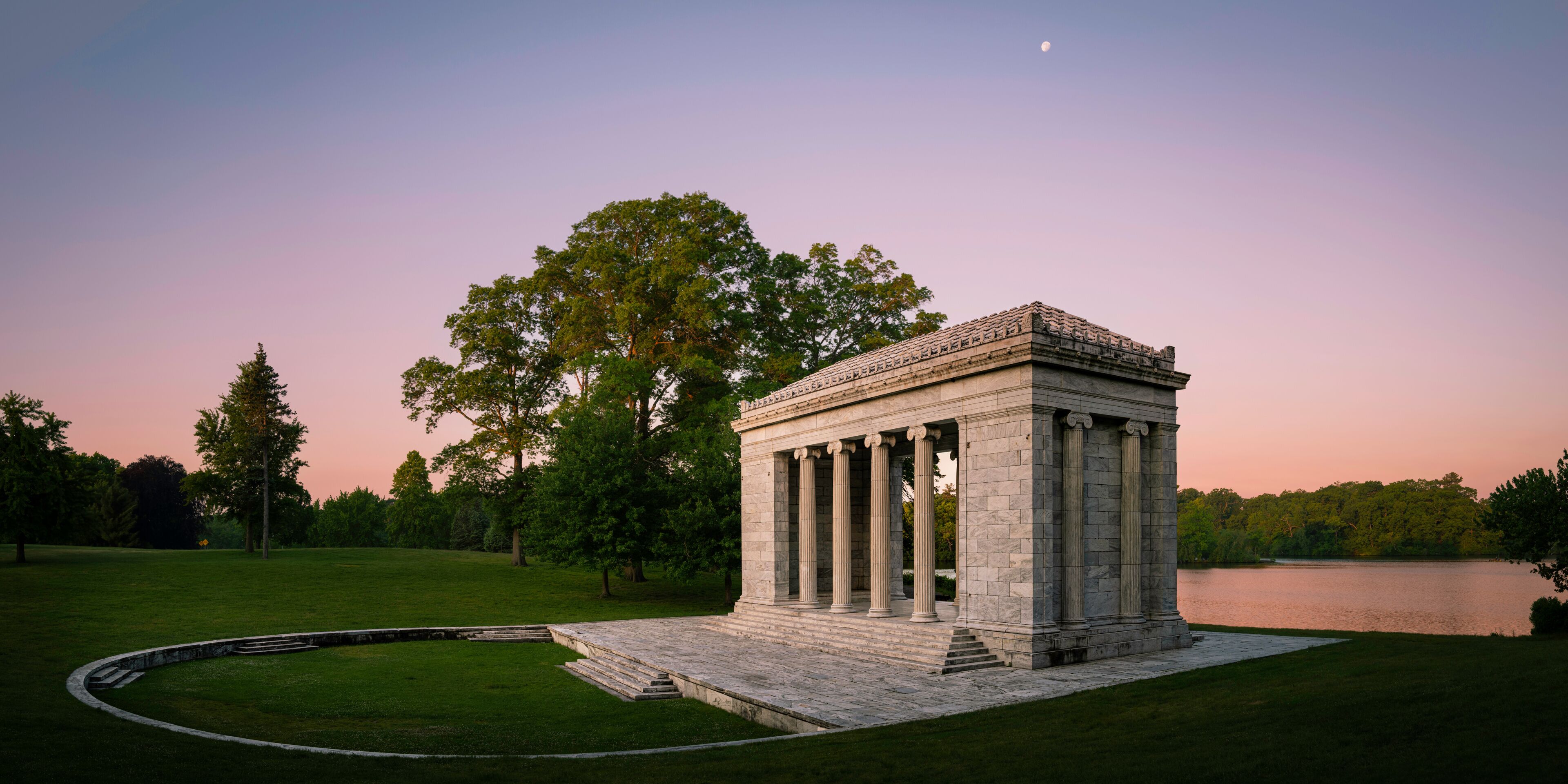 Tranquil sunset moon rising landscape at Temple to Music Pavilion and meadow forest park at Roger Williams Park in Providence, Rhode Island, pink horizon and water reflections on Cunliff Lake