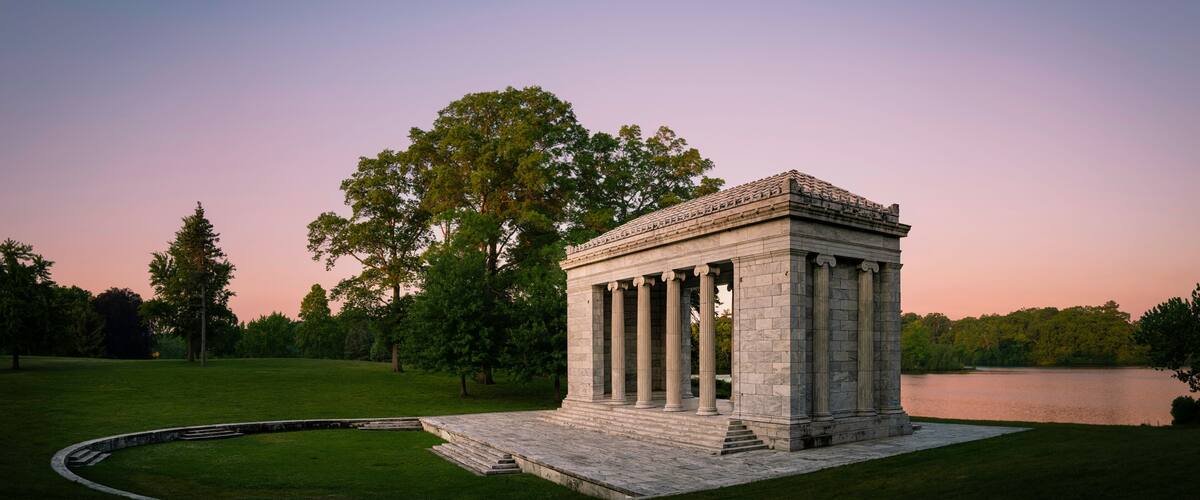 Tranquil sunset moon rising landscape at Temple to Music Pavilion and meadow forest park at Roger Williams Park in Providence, Rhode Island, pink horizon and water reflections on Cunliff Lake