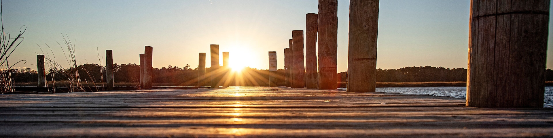 Um cais de madeira com estacas que se estendem sobre a água ao pôr do sol.