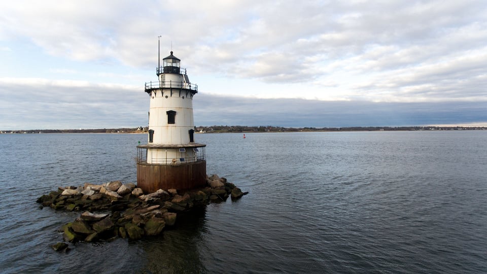 A lighthouse on a rocky outcrop in a body of water with a cloudy sky.