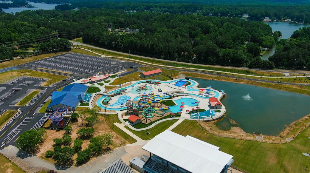 a stunning aerial shot of long winding pools with blue water and colorful waterslides with a lake with a water fountain surrounded by lush green trees and grass at Lake Spivey Recreation Center