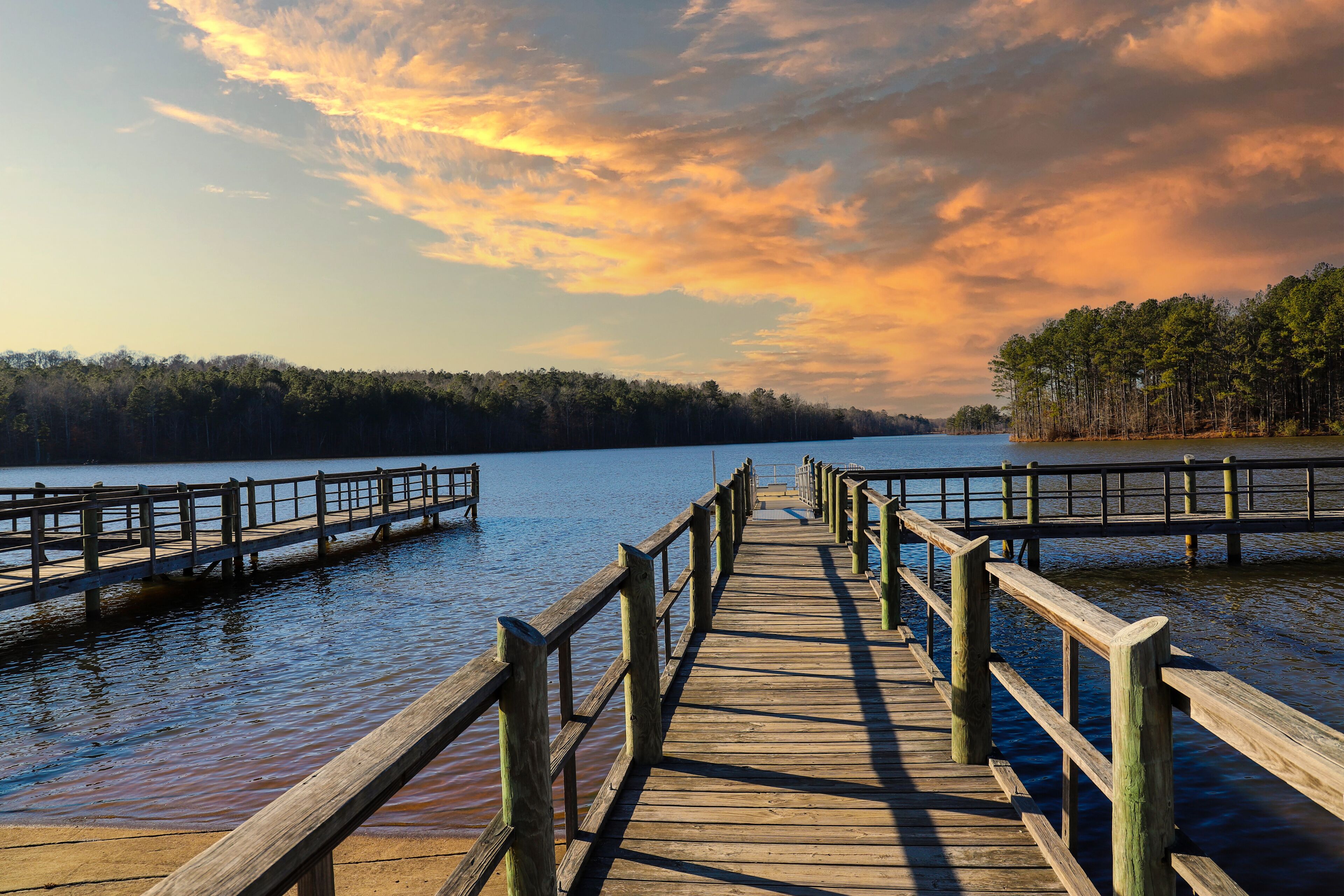 a long gray wooden bridge on the vast blue lake water of Lake McIntosh with stunning skies and lush green and autumn colored trees on the banks of the lake at Lake McIntosh in Peachtree City Georgia