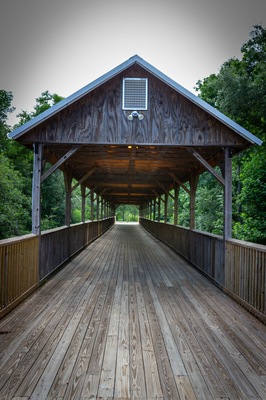 A wooden, covered bridge with green trees in the background.