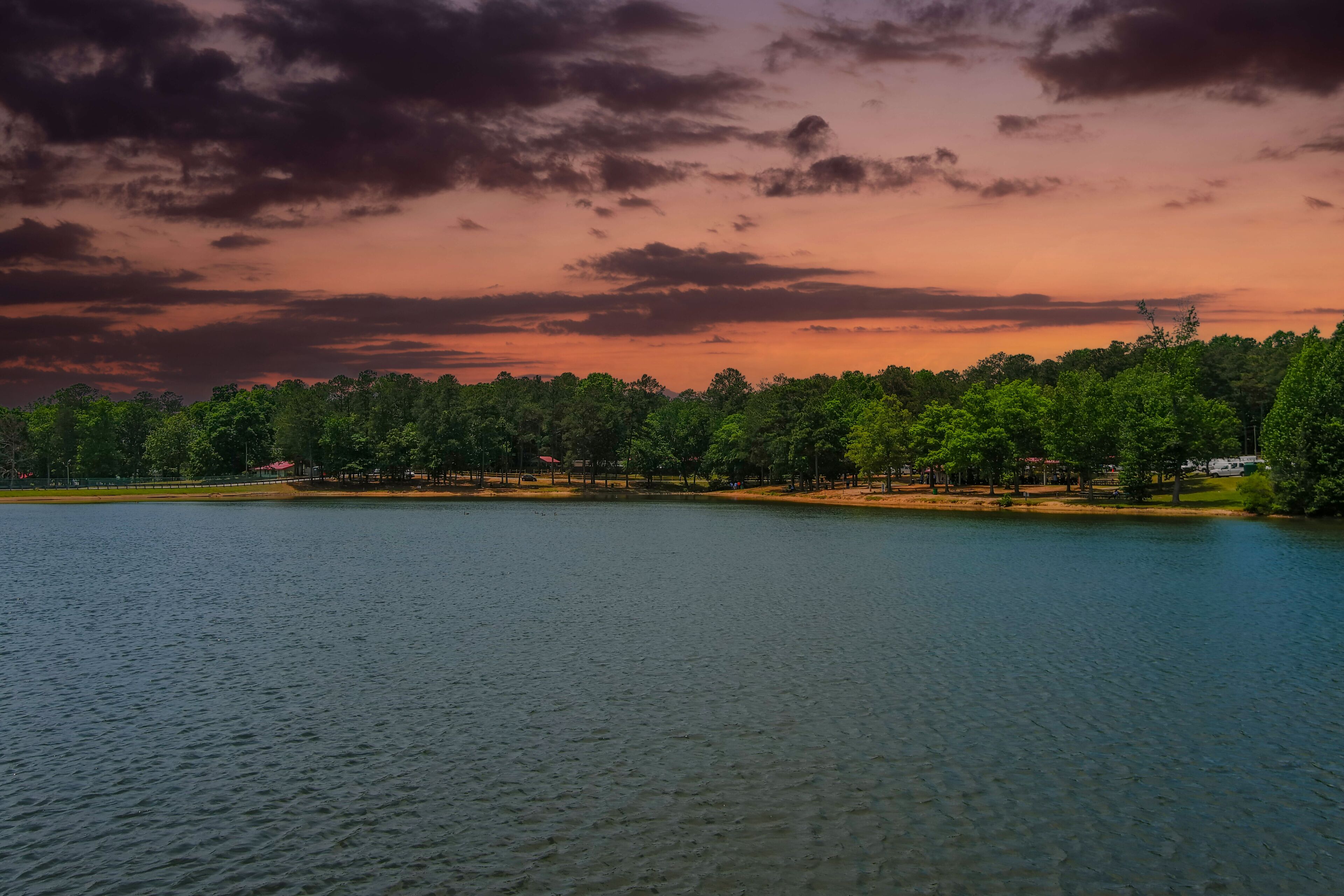 a gorgeous blue rippling lake surrounded by lush green trees, grass and plants with powerful red clouds at sunset at Lake Spivey Recreation Center in Jonesboro Georgia USA
