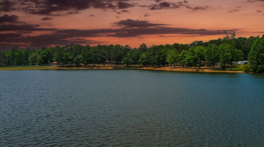 a gorgeous blue rippling lake surrounded by lush green trees, grass and plants with powerful red clouds at sunset at Lake Spivey Recreation Center in Jonesboro Georgia USA