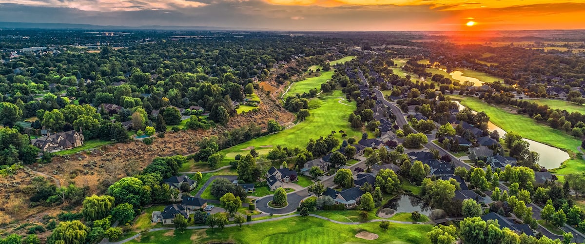 A golf course with houses, trees, and a sunset.