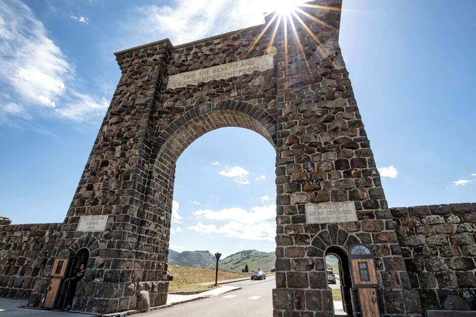 A stone archway with inscriptions, surrounded by a road and a mountainous landscape.