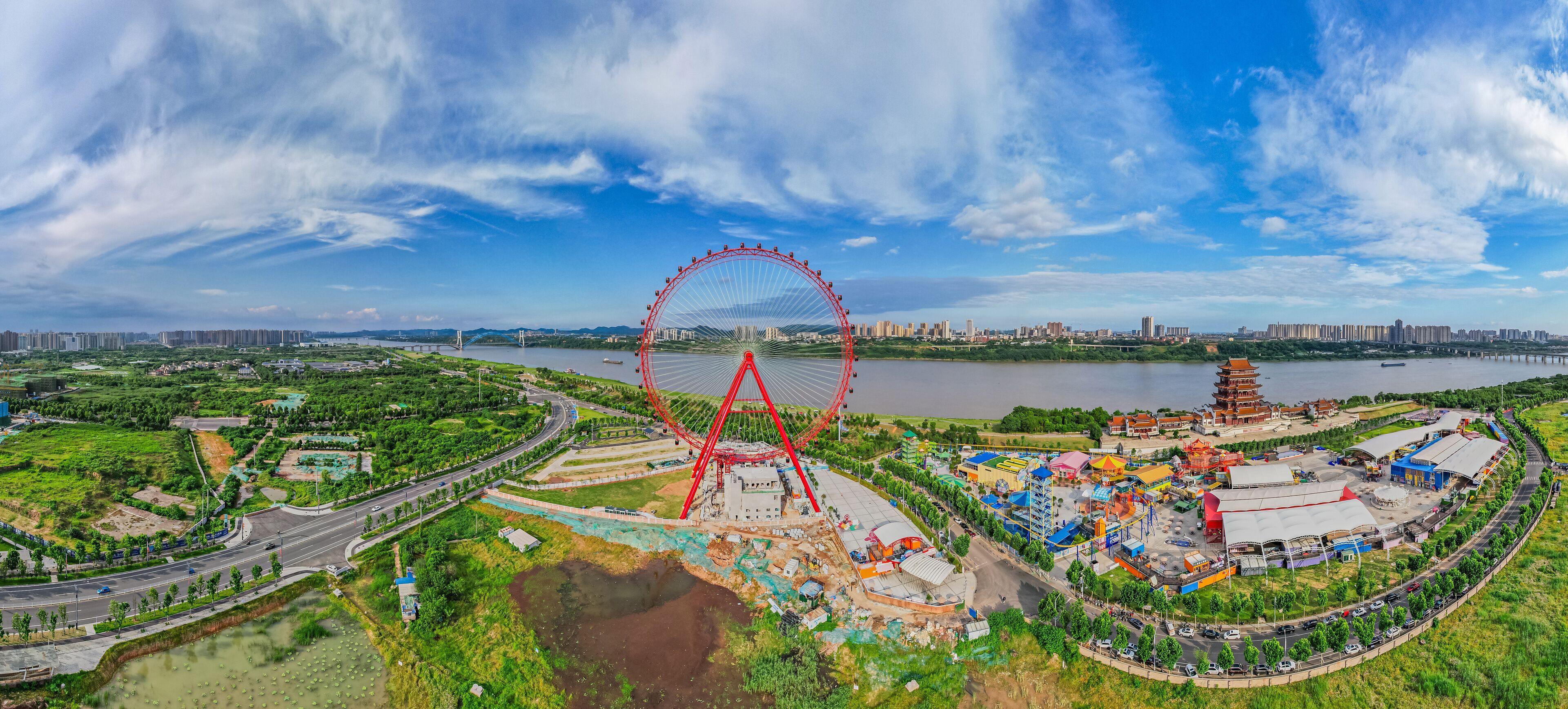 A large Ferris wheel, a river, and a city skyline in the background.