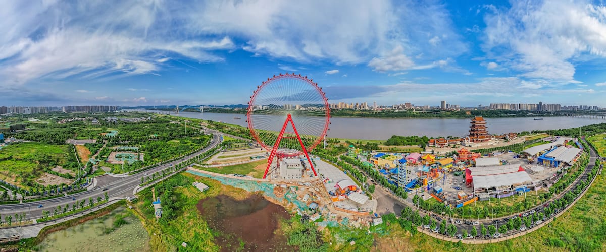 A large Ferris wheel, a river, and a city skyline in the background.
