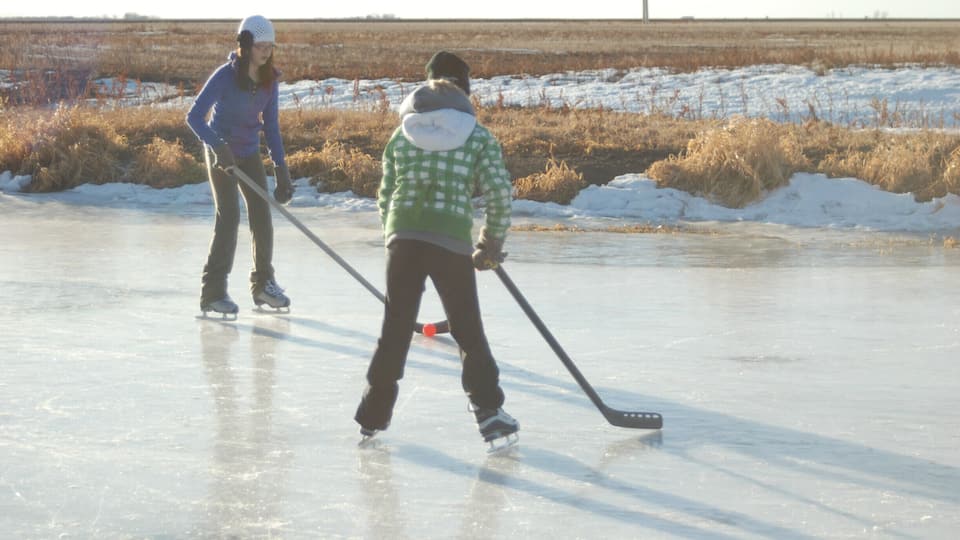 Two people ice skating on a frozen lake with a distant field in the background.
