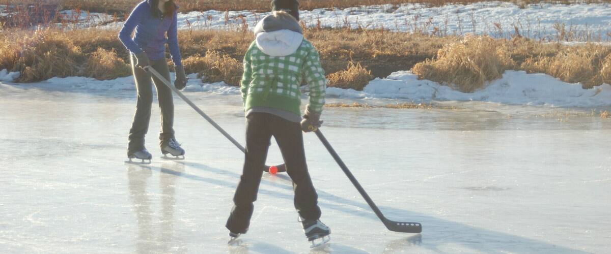 Two people ice skating on a frozen lake with a distant field in the background.