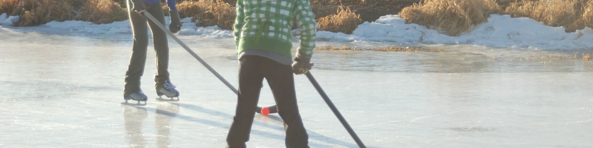 Two people ice skating on a frozen lake with a distant field in the background.