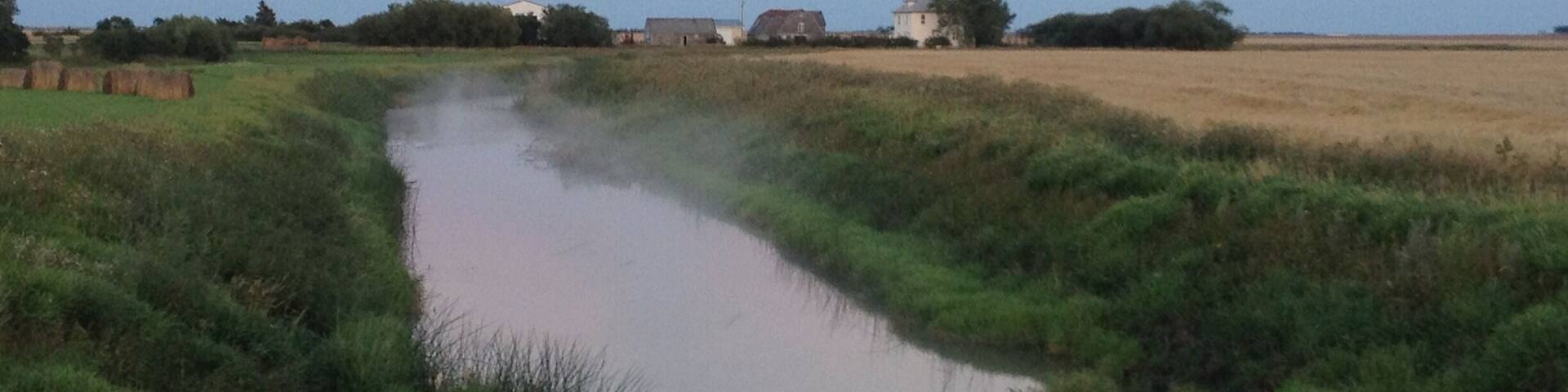 Mist on the creek that goes past a cute prairie farm house