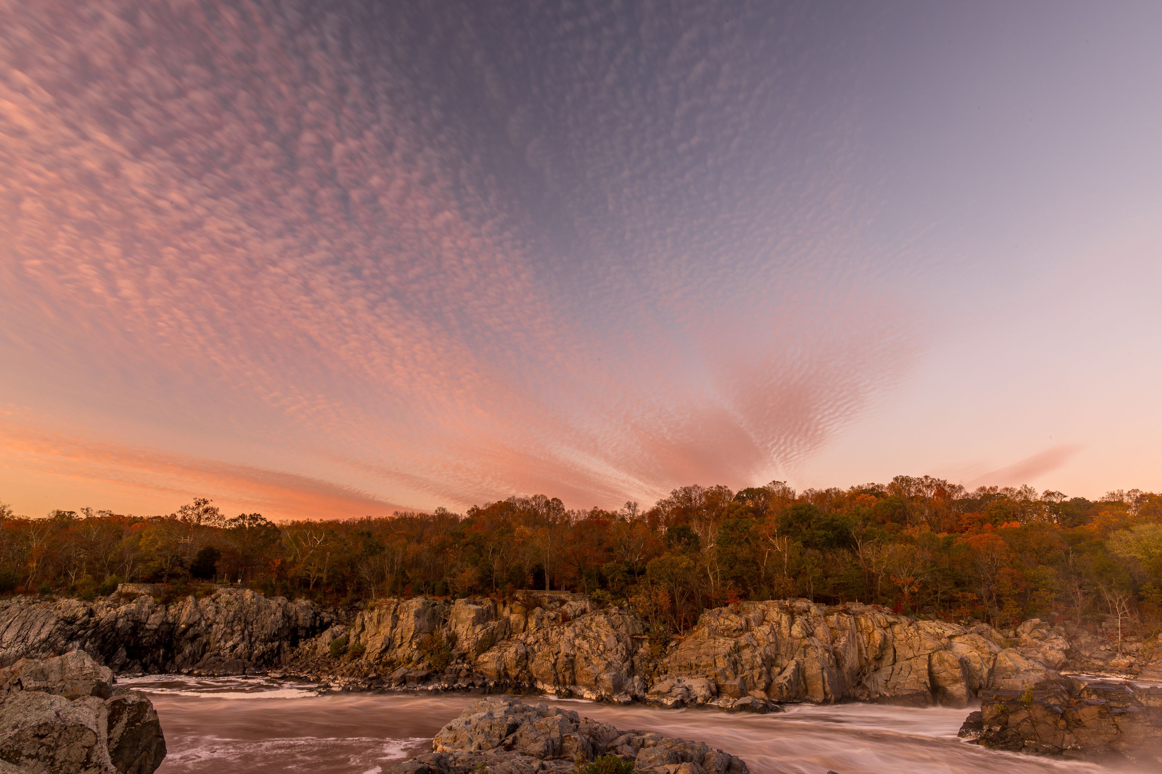 A river flowing through a rocky landscape with autumn-colored trees in the background.