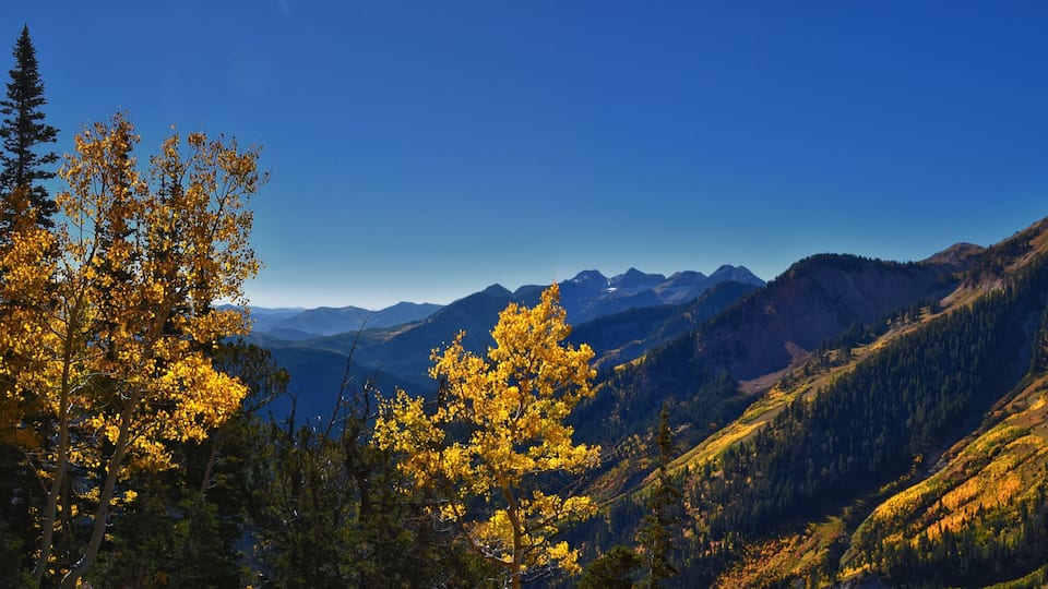 A mountain range with autumn foliage, clear skies, and distant peaks.
