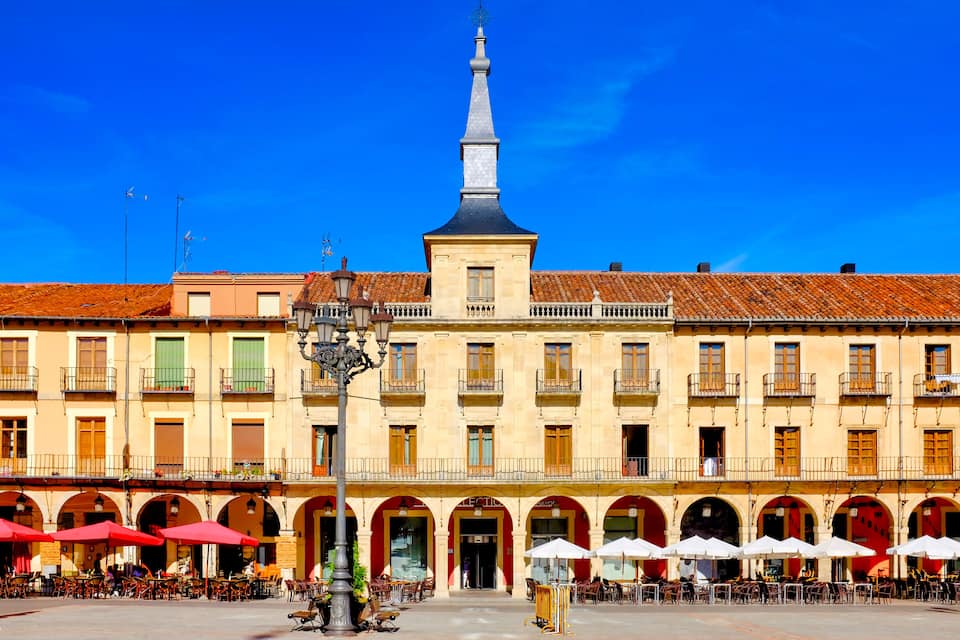 A historic square with a prominent church tower, red-roofed buildings, and outdoor cafes.