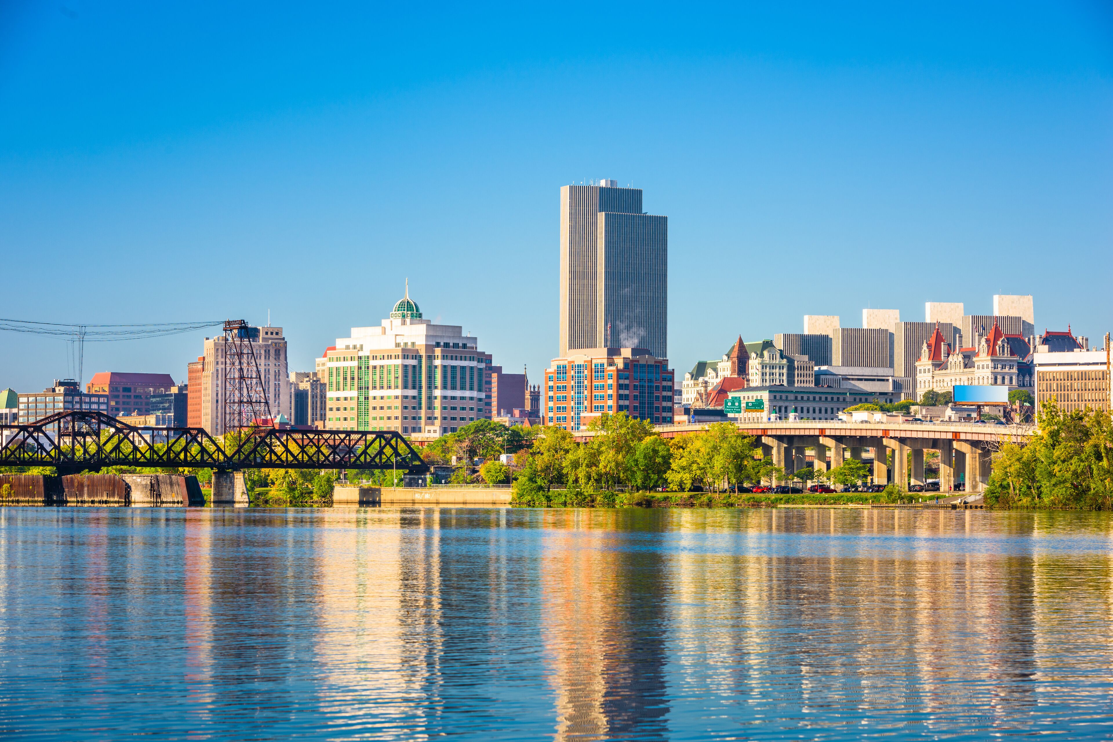 A city skyline with a river in the foreground, a bridge, and various buildings including a tall skyscraper.