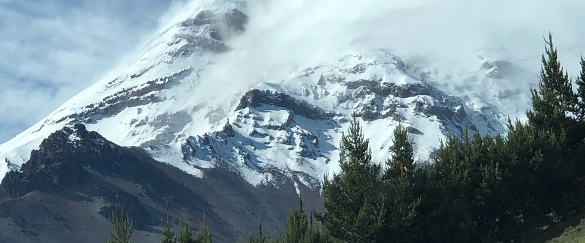 A snow-covered mountain with a peak partially obscured by clouds.