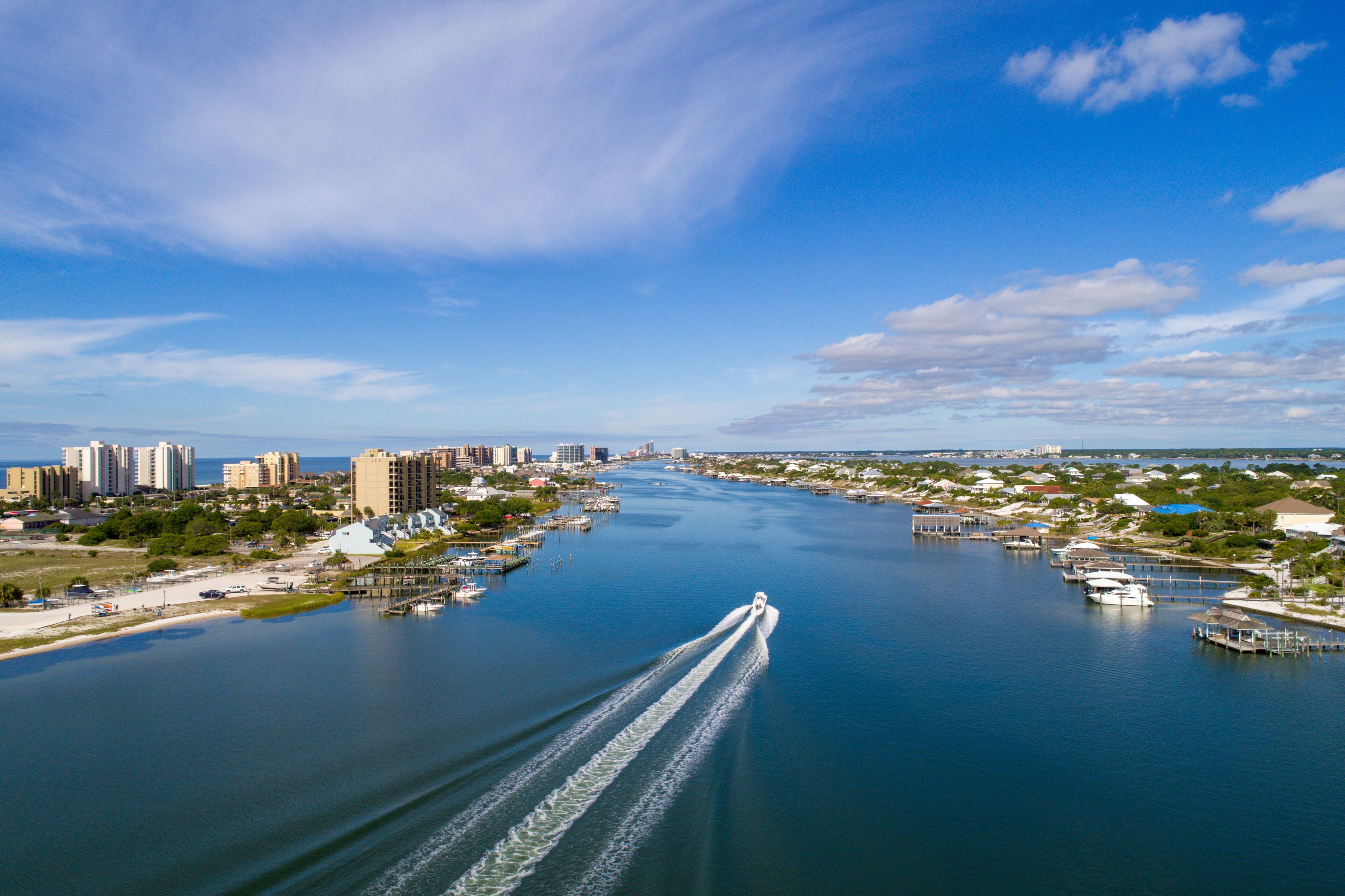 A river with a boat creating a wake, surrounded by buildings and docks.