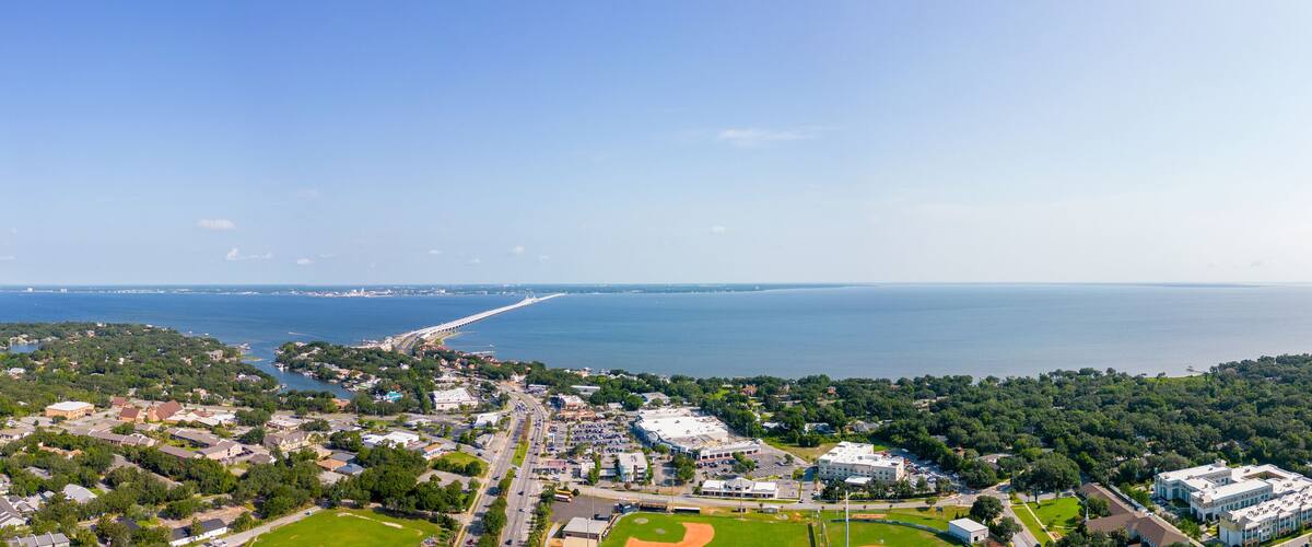 A coastal town with a marina, a long pier, and a baseball field.