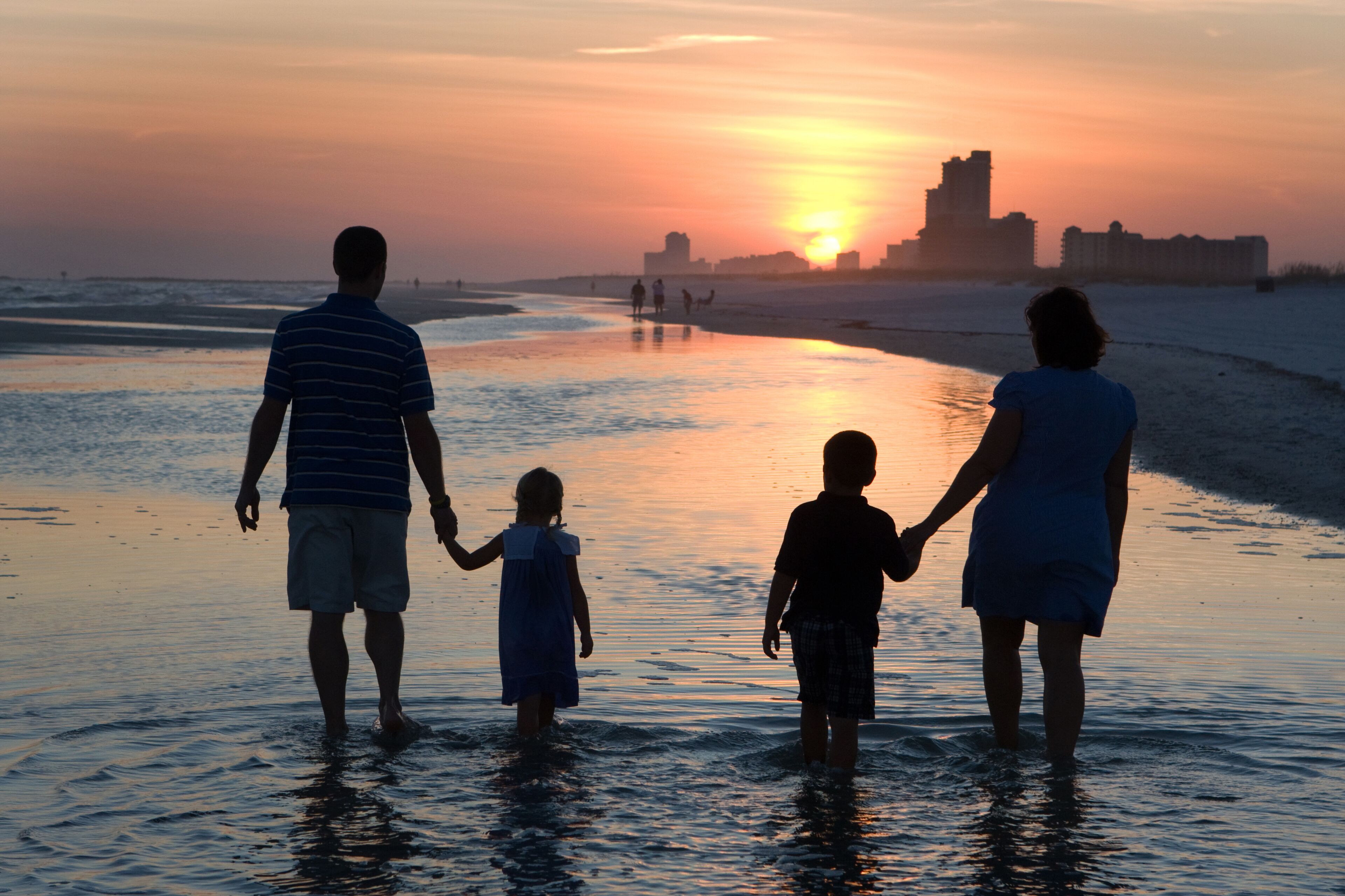 A sunset over a beach with people walking in the water.