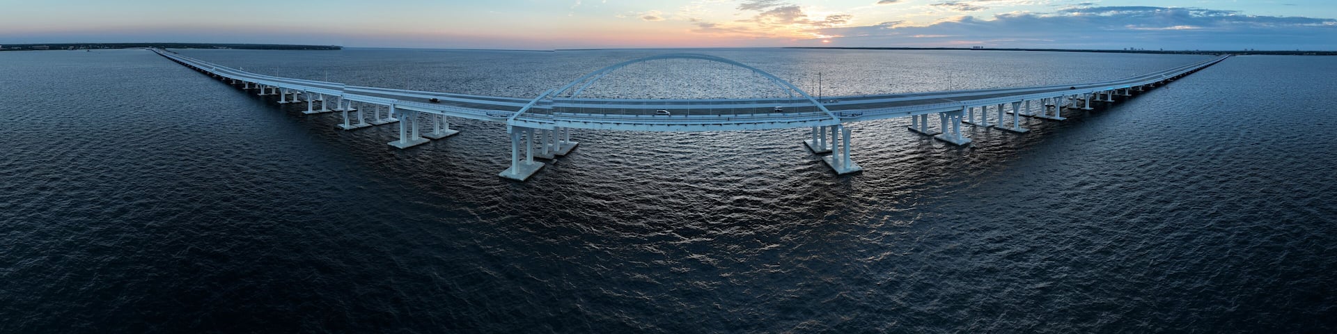 A large suspension bridge over a body of water with a sunset in the background.