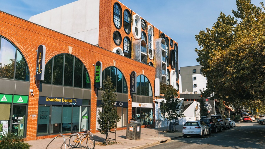 A multi-story building with a brick facade, large arched windows, and signage for businesses including a dental surgery and a bike shop.