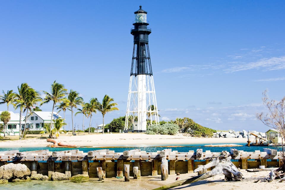 A lighthouse, palm trees, a beach, and a rocky shoreline.