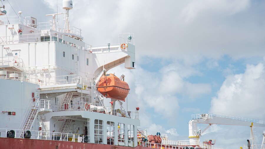 Close-up bridge deck, crane, lifeboat VHF radio frequencies antennas satellite signals navigation radar on large crude oil tanker bulk transport sail thru South Padre Island, Brownsville port, TX