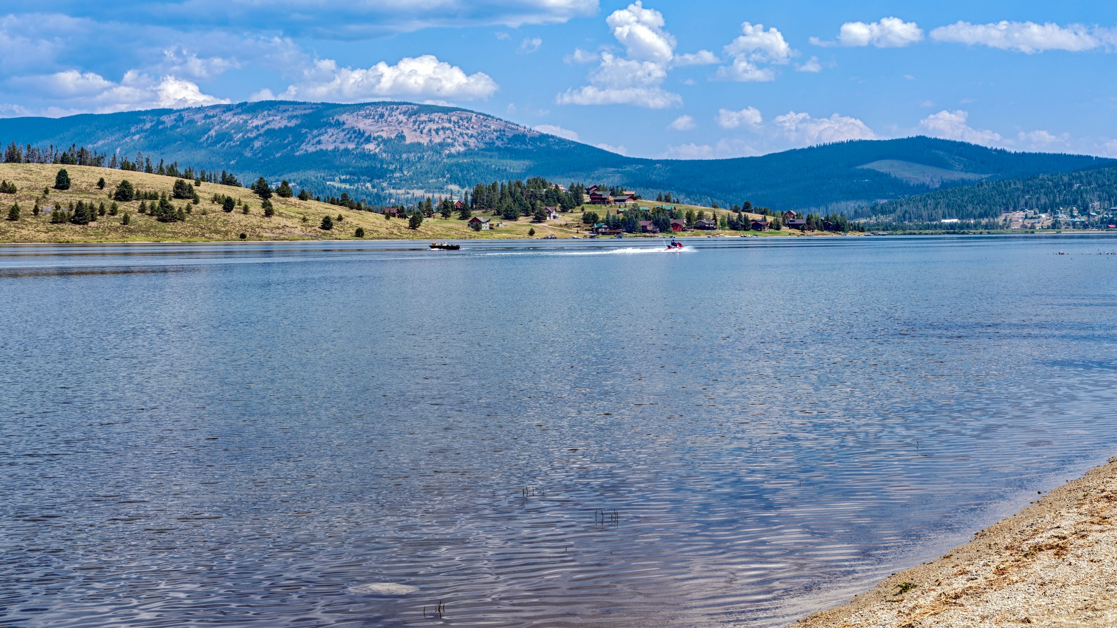 A calm lake with a boat, surrounded by mountains and houses.